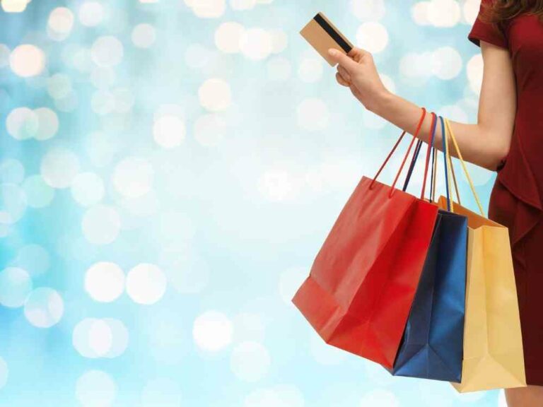 Woman holding a credit card and shopping bags in front of a blue backgroun
